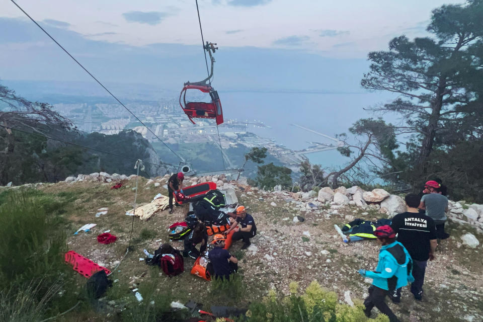 Rescue and emergency team members work with passengers of a cable car transportation system outside Antalya, southern Turkey, Friday, April 12, 2024. At least one person was killed and several injured Friday when a cable car pod in southern Turkey hit a pole and burst open, sending the passengers plummeting to the mountainside below, officials and local media said. Scores of other people were left stranded late into the night after the entire cable car system came to a standstill. (Dia Images via AP)