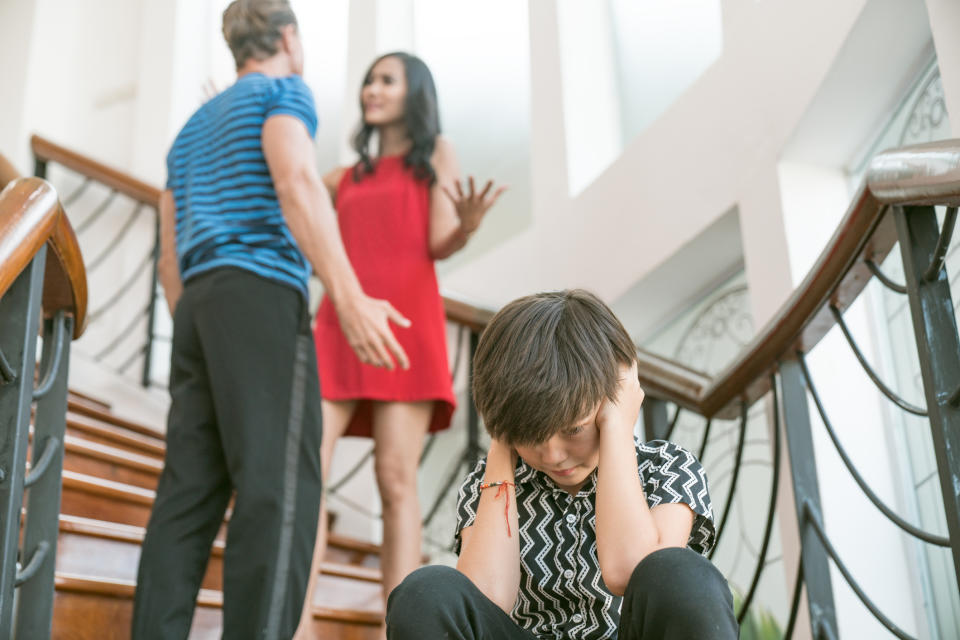 kid covering his ears as parents fight behind him