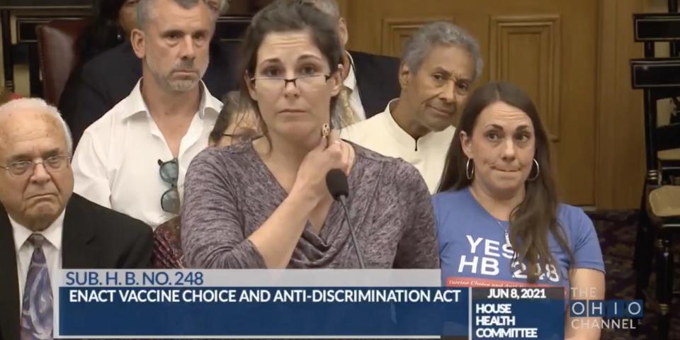 A nurse at the Ohio Statehouse hearing holding a key to her neck while the audience looks skeptically on.