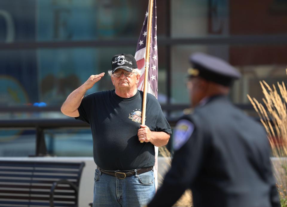 A man holding the U..S. Flag keeps a salute up as officers head to their cars to start a procession to the cemetery during the funeral of Rochester officer Anthony Muzurkiewicz.
