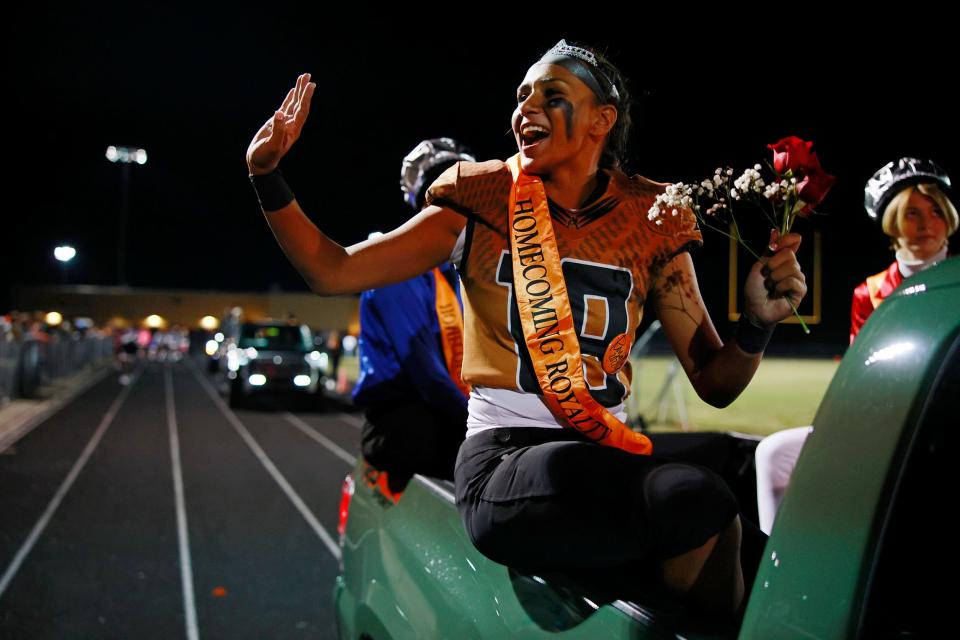 Gaby Rourke (19) waves to the crowd after being honored formally for being named Junior Homecoming Queen riding in a truck with Junior Homecoming King Malachi Bryant, back, and Junior Homecoming Sovereign Zachirey Hunt, right, at Friday's game against Raines.