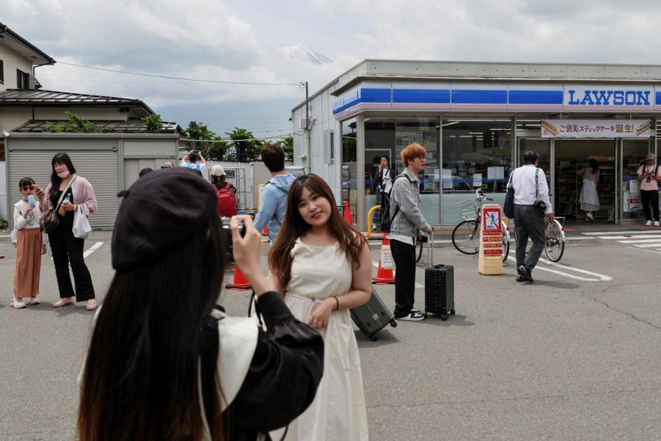 A tourist poses for a photo of Mount Fuji appearing above a convenience store after a barrier was installed to block off the popular tourist spot, in Fujikawaguchiko (Reuters)