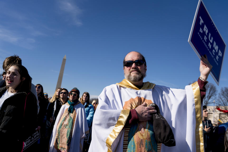 FILE - In this Friday, Jan. 19, 2018 file photo, Brother Tomasio Venditti of Steubenville, Ohio, right, holds a Trump-Pence campaign sign as he and Lis Kelly of Notre Dame, Ind., background, wear white gowns depicting the Lady of Guadalupe during an anti-abortion rally on the National Mall in Washington during the annual March for Life. The annual march to proteststhe Supreme Court's landmark 1973 decision that declared a constitutional right to abortion. (AP Photo/Andrew Harnik)