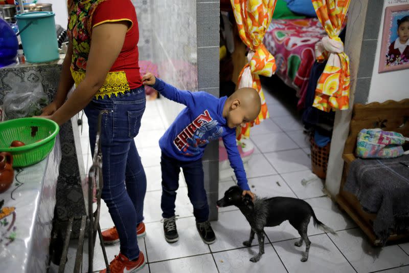 Hermes Soto pets Wicha the dog as he touches his mother, Esperanza Paz, at their house in Mexico City