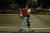 A migrant carrying a young child walks before dawn along the highway to Choloma, Honduras, Thursday, Jan. 14, 2021. About 200 Honduran migrants resumed walking toward the U.S. border, a day before a migrant caravan was scheduled to depart San Pedro Sula. (AP Photo/Delmer Martinez)