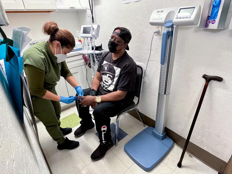 A health worker removes a pulse oximeter from a patient's index finger after taking his blood pressure.