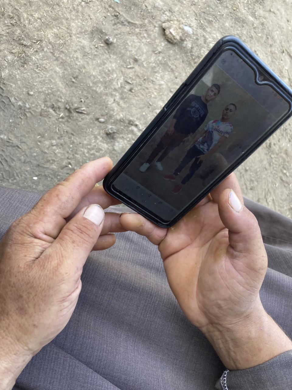 Ashraf Sadawy Abdel-Fattah holds his phone and looks at a picture of two of his sons who died in flooding in the Libyan city of Derna, Mohamed Ashraf 23, his second-oldest, and Abdel-Rahman, 19, as he sits outside his home in the farming village of Nazlet el-Sharif, Egypt, Thursday Sept. 14, 2023. The village is mourning the deaths of dozens of its men in the floodwaters that tore through a city in neighboring Libya. At least 74 bodies were brought back earlier this week for burial. (AP Photo/Samy Magdy)