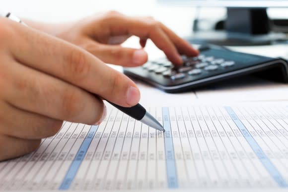 An accountant examining figures with the aid of a calculator.