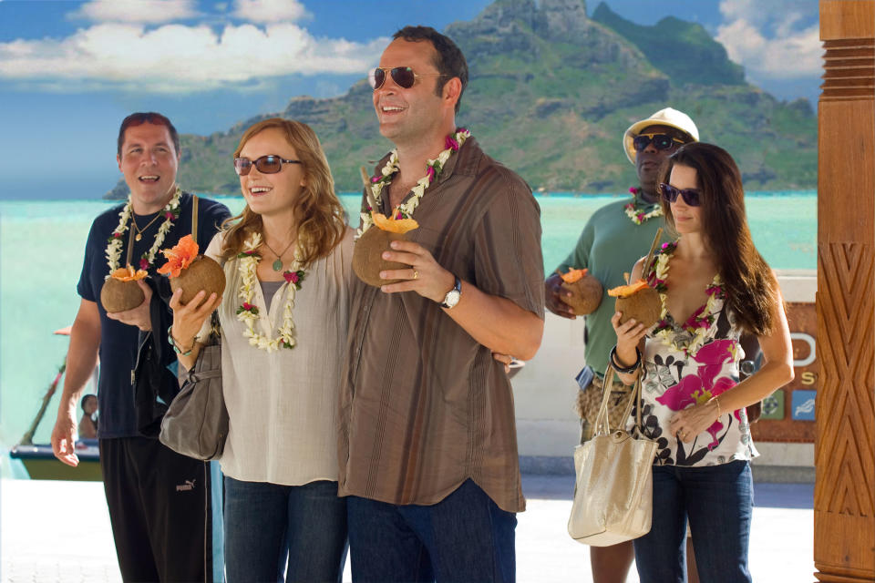 Group shot of people, including Jason Bateman, Kristen Bell, and Vince Vaughn, standing together on a tropical vacation, enjoying coconut drinks and leis