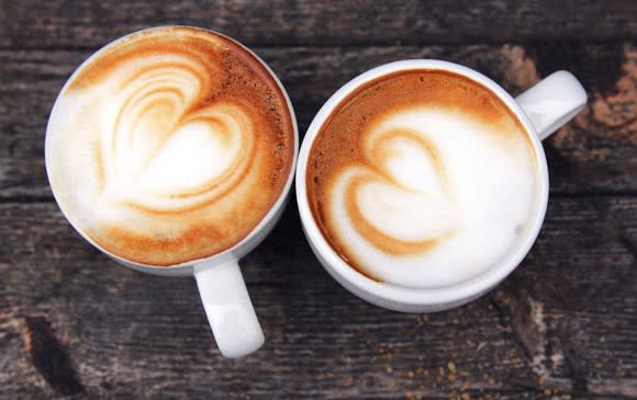 Two coffee cups topped with milk froth on a wooden table