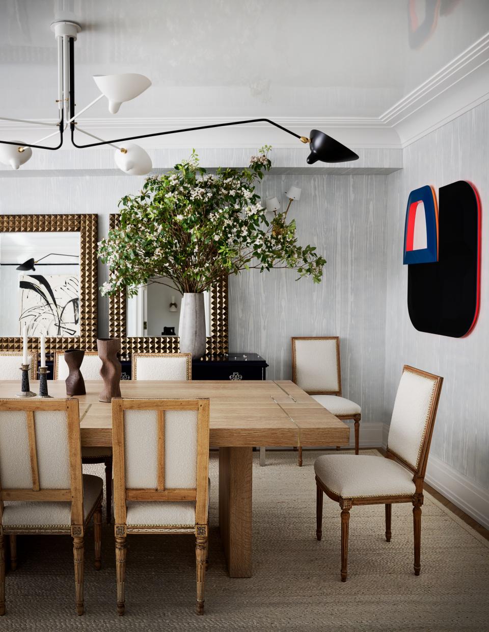 Jansen chairs pull up to a custom oak dining table surrounded by faux bois wallpaper by Holland & Sherry. Serge Mouille chandelier; mirrors from Newel; painting by Beverly Fishman.