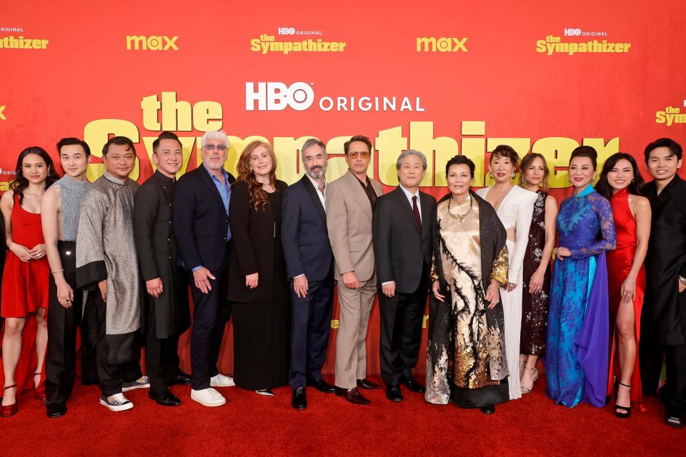 At the Los Angeles premiere of "The Sympathizer" on April 9, 2024, actress Kieu Chinh, wearing a gold-and-black traditional Vietnamese ao dai, stands between co-star Sandra Oh and director Park Chan-wook, who's next to co-executive producer Robert Downey Jr. The miniseries is based on a best-selling novel by Viet Thanh Nguyen, standing under the letter "h."