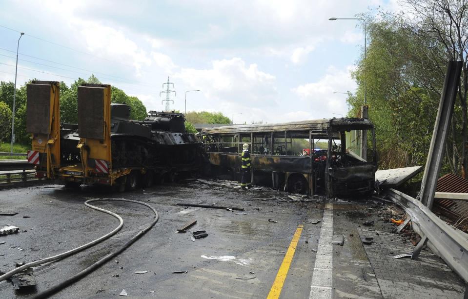 In this handout photo provided by Hasicsky Zachrany Sbor or HZS Praha, Czech Republic's firefighters investigate a scene of a crash in Prague, Czech Republic, Thursday, May 2, 2019. Czech firefighters and police say a bus with prisoners caught fire after colliding with two trucks, one of them carrying two tanks. The Prague rescue service says one person has died in the crash that occurred on Thursday on a busy ring road that leads to Prague's international airport. (HZS Praha via AP)