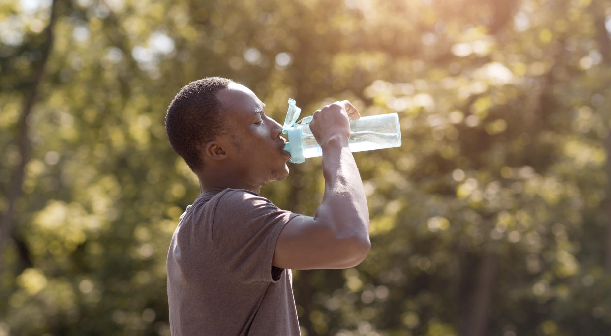 Overheated black guy drinking water from bottle in park, free space