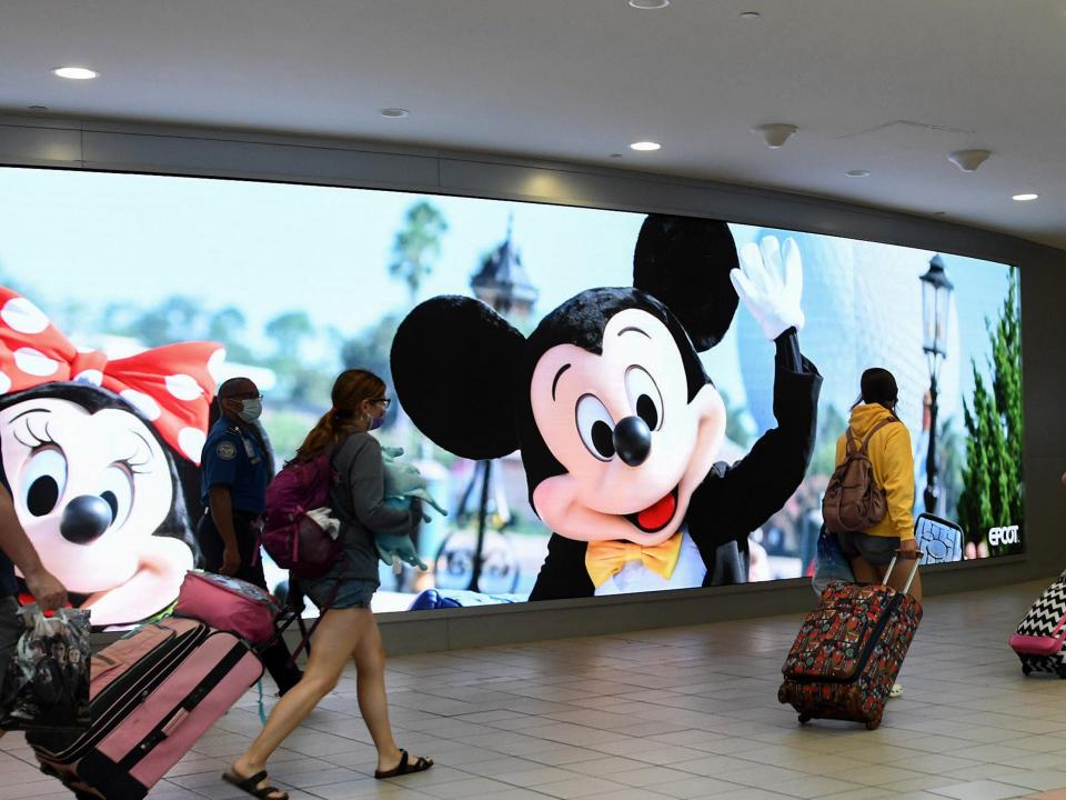 Travelers walk past a sign advertising Walt Disney World at Orlando International Airport as the July 4th holiday weekend begins. Americans are expected to travel in record numbers over the Independence Day holiday.