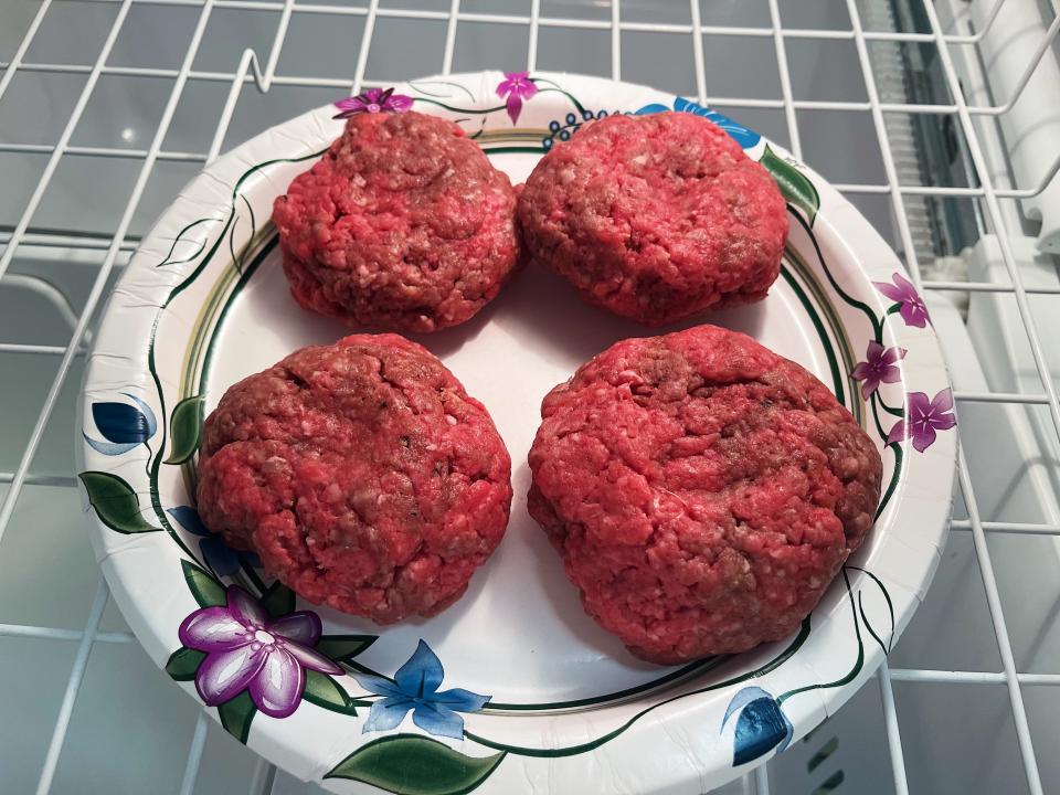 four uncooked hamburger patties on a paper plate in a freezer