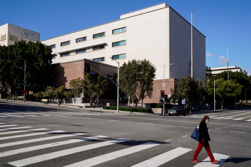 LOS ANGELES, CA - MARCH 21: A pedestrian in a face mask walks in a crosswalk with the Stanley Mosk Superior Court behind them in downtown Los Angeles is photographed on Saturday, March 21, 2020 in Los Angeles, CA. Earlier in the week, California Governor Gavin Newsom issued a "Safer at Home" order to the entire state to help slow the spread of the Coronavirus as it sweeps across the world. (Kent Nishimura / Los Angeles Times)