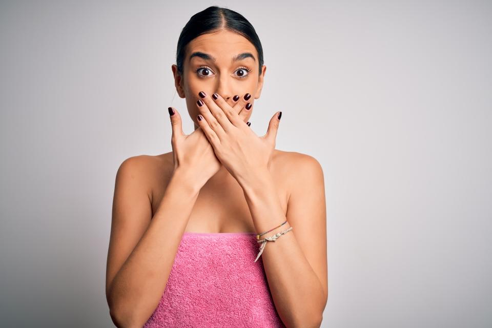 Young beautiful brunette woman wearing towel after shower over isolated white background shocked covering mouth with hands for mistake. Secret concept.