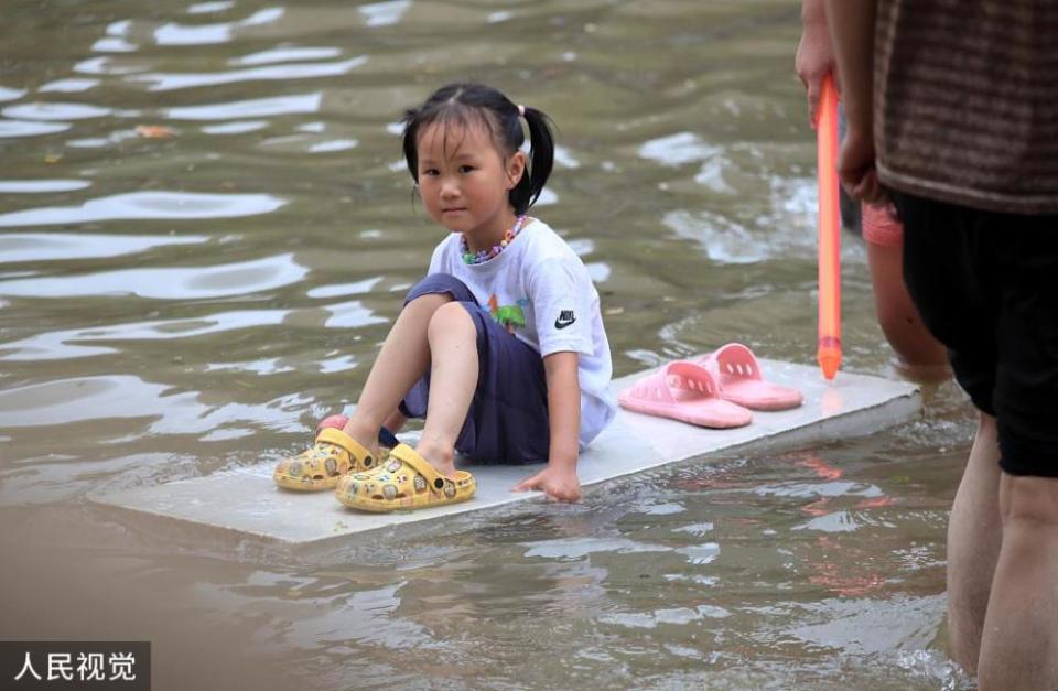 鄭州一名女學童坐在木板上，在淹水的街道中漂浮。   圖：翻攝自人民視覺