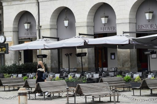 Two women walk past deserted restaurants in Milan's empty Piazza della Scala on February 29