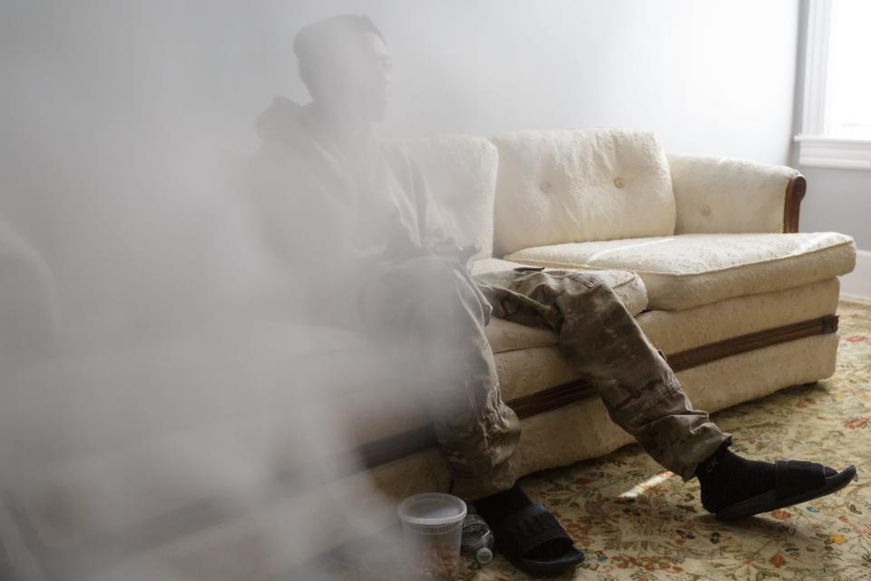 A man is seen, obscured behind a curtain, sitting on a couch.