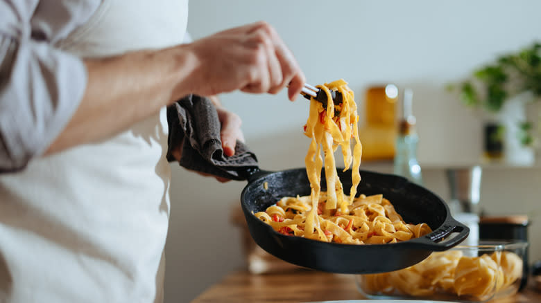 chef tossing pasta in skillet