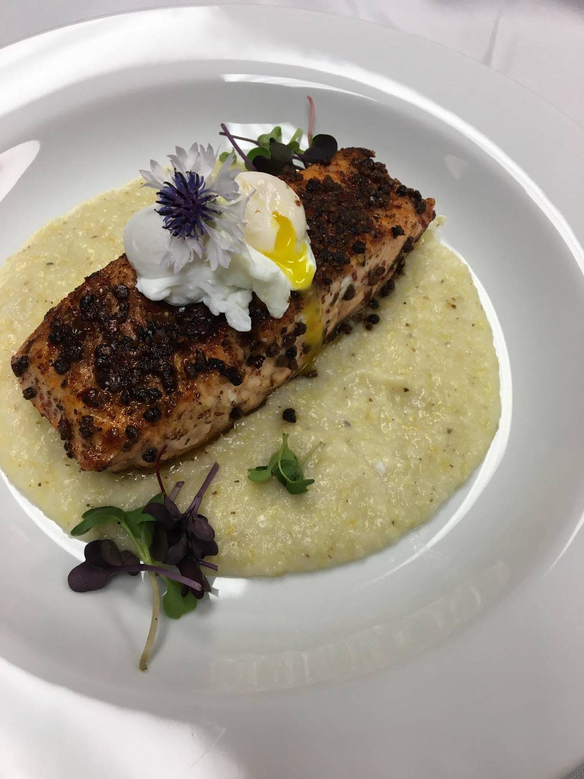 A pink peppercorn crusted salmon with grits and a poached quail egg, a catering food option from Root 76 Cuisine.