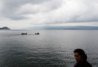 Rescue team members are seen on boats as Kamel Purba, a farmer who lost his mother and brother in the ferry accident at Lake Toba, sits on a pier of Tigaras port in Simalungun, North Sumatra, Indonesia June 21, 2018. REUTERS/Beawiharta