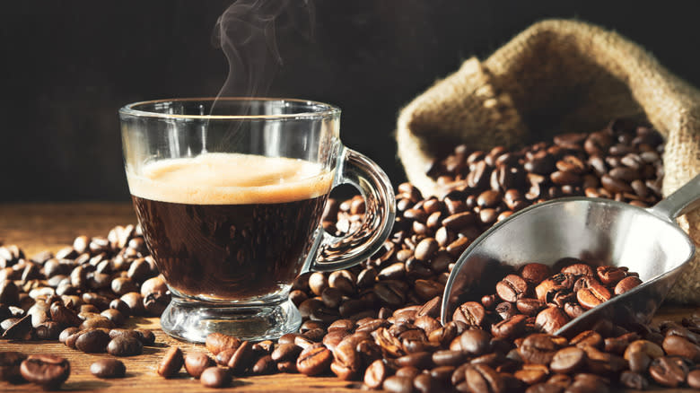 Foamy coffee in glass cup surrounded by beans