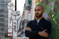 Jad al-Rayess, a Lebanese anti-government activist, stands in front of large cardboard fist labelled: "Revolution," background, in Beirut, Lebanon, Wednesday, Nov. 18, 2020. A year after anti-government protests roiled Lebanon, dozens of protesters are being tried before military courts that human rights lawyers say grossly violate due process and fail to investigate allegations of torture and abuse. (AP Photo/Hussein Malla)