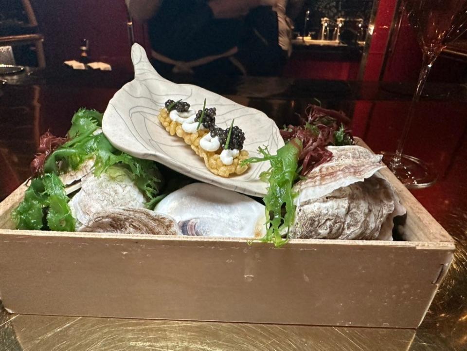 A white leaf-shaped tray with a cracker topped with caviar on it