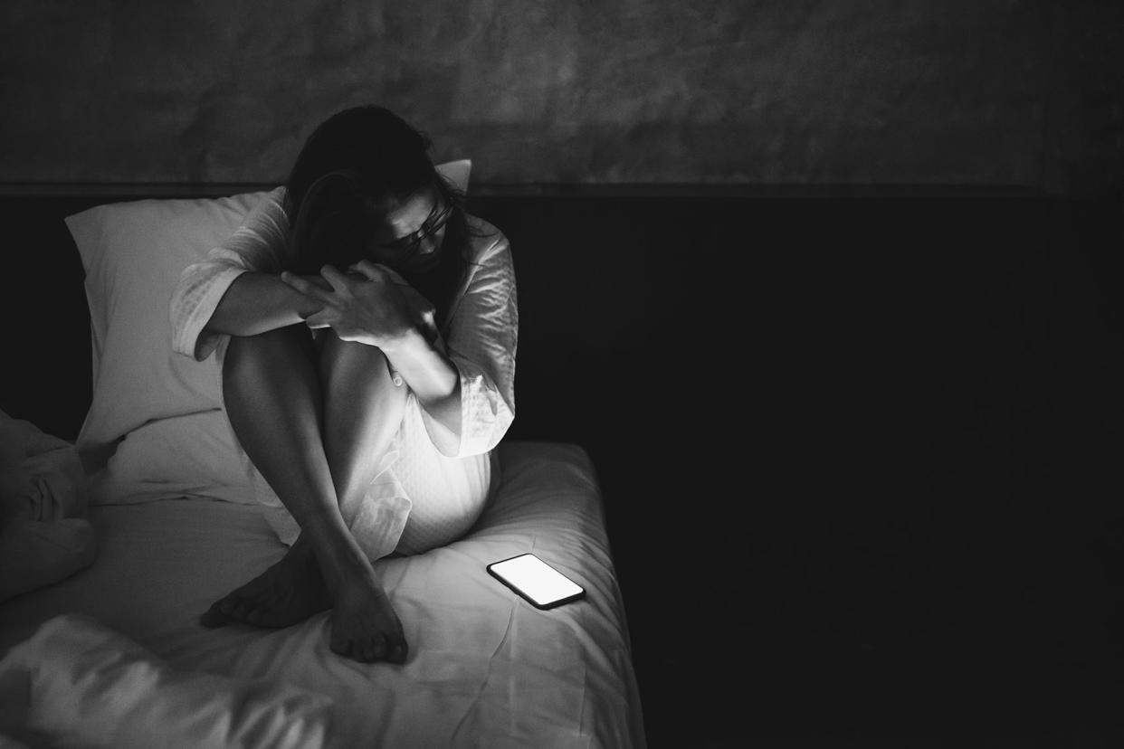 Sad woman staring at phone bedGetty Images/Boy_Anupong