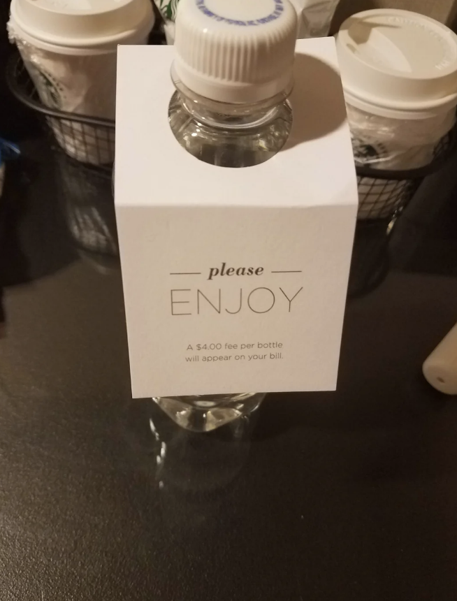 Water bottle with a note: "Please enjoy. A $4.00 fee per bottle will appear on your bill."