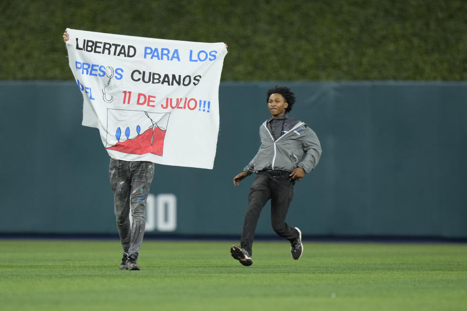 A security guard prepares to take out a demonstrator that ran onto the field during the sixth inning of a World Baseball Classic game between Cuba and the U.S., Sunday, March 19, 2023, in Miami. (AP Photo/Wilfredo Lee)