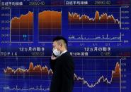 A man wearing a protective mask, amid the coronavirus disease (COVID-19) outbreak, walks past an electronic board displaying graphs (top) of Nikkei index outside a brokerage in Tokyo