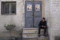 A Palestinian man sits in front of doors plastered with posters showing Ammar Adili, 22, who was shot and killed by an Israeli border police officer on Friday, in his home village of Osreen, south of the West Bank city of Nablus, Saturday, Dec. 3, 2022. Palestinians pushed back Saturday against Israeli police claims that Ammar Adili had attacked Israelis, including a border policeman, in the area and that he was shot in self-defense. They said the officer killed Adili without cause, and that Palestinian medics were kept from trying to save him as he lay gravely wounded on the side of a busy throughfare in the occupied West Bank town of Hawara. (AP Photo/Nasser Nasser)