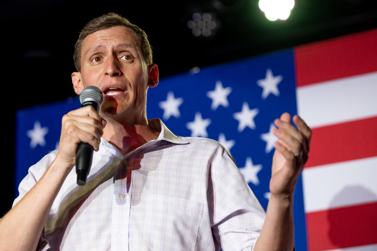 Blake Masters speaks into a microphone while standing in front of an American flag.