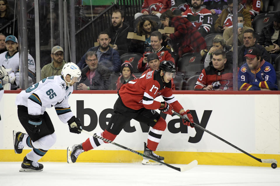 New Jersey Devils center Yegor Sharangovich (17) skates with the puck as he is pursued by San Jose Sharks defenseman Erik Karlsson (65) during the first period of an NHL hockey game Tuesday, Nov. 30, 2021, in Newark, N.J. (AP Photo/Bill Kostroun)