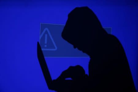 A hooded man holds a laptop computer as blue screen with an exclamation mark is projected on him in this illustration picture taken on May 13, 2017. REUTERS/Kacper Pempel/Illustration