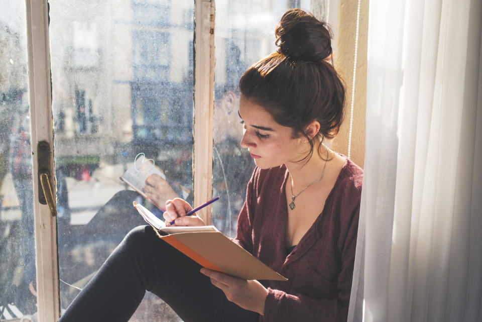 Young woman writes next to the window to ease broken heart.