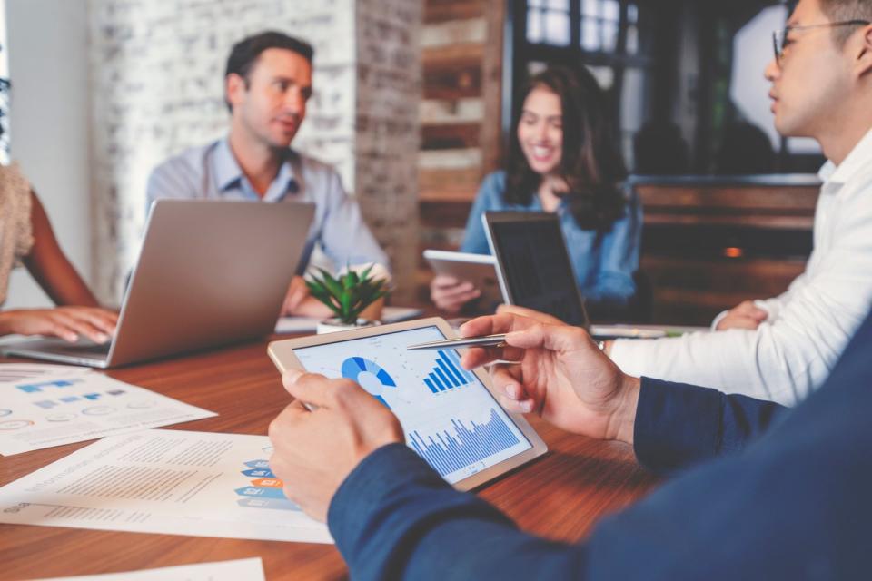 Employees analyzing financial metrics using tablets and laptops while seated in a conference room.