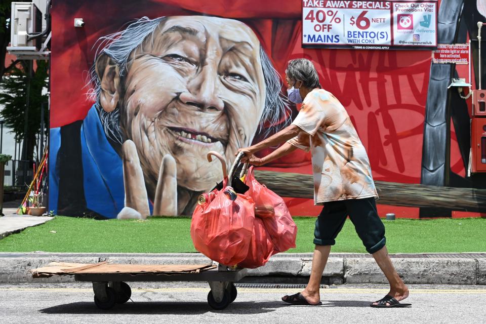 An elderly woman wearing a protective facemask amid fears about the spread of the COVID-19 coronavirus pushes cart past a wall mural of an elderly person in Singapore on May 8, 2020. 