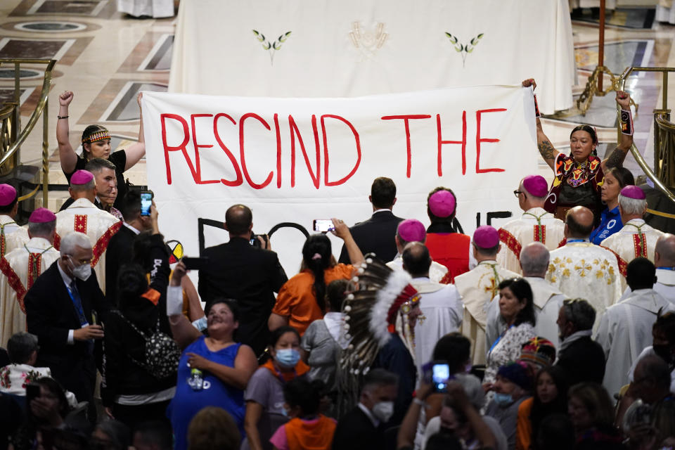 Protesters hold up a banner during a mass with Pope Francis at the National Shrine of Saint Anne de Beaupre, Thursday, July 28, 2022, in Saint Anne de Beaupre, Quebec. Pope Francis is on a "penitential" six-day visit to Canada to beg forgiveness from survivors of the country's residential schools, where Catholic missionaries contributed to the "cultural genocide" of generations of Indigenous children by trying to stamp out their languages, cultures and traditions. (AP Photo/John Locher)