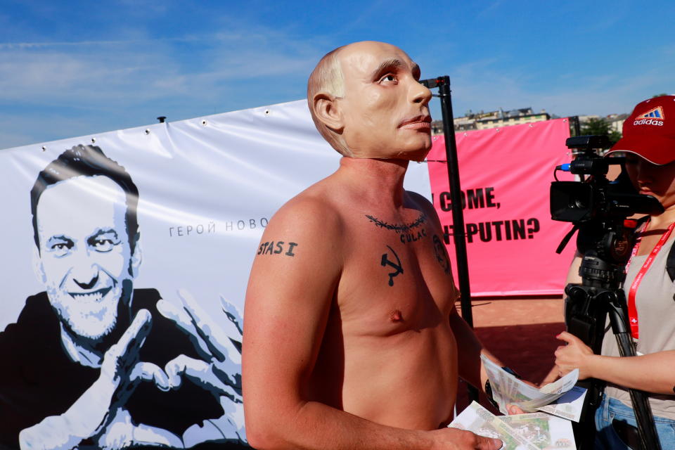 A protester wearing a mask of Russian President Vladimir Putin throws fake bank notes in front of a poster of Alexei Navalny ahead of a meeting between U.S. President Biden and Russian President Putin in Geneva