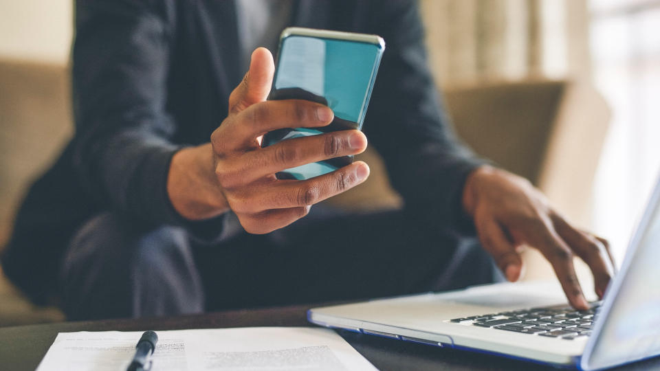 Cropped shot of an unrecognizable man using a smartphone and a laptop while working from home.