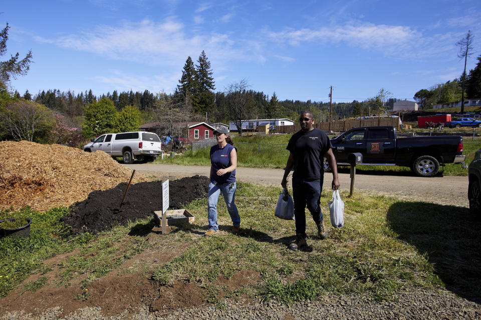 Melynda Small, left, and Marc Brooks, founder of Cascade Relief Team, walk to the Landscaping With Love greenhouse in Otis, Ore., on Thursday, May. 13, 2020. The greenhouse provides landscaping materials free to residents, helping the small town on the Oregon coast recover from the devastating fire that destroyed 293 homes. (AP Photo/Craig Mitchelldyer)