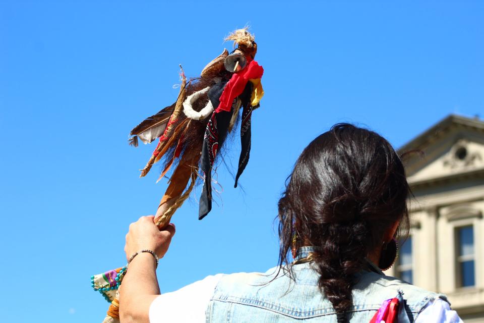 Dawne DuShane holds a staff bearing eagle feathers and the colors of the Anishinaabe on Longest Walk 5 on June 17, 2022, at the State Capitol