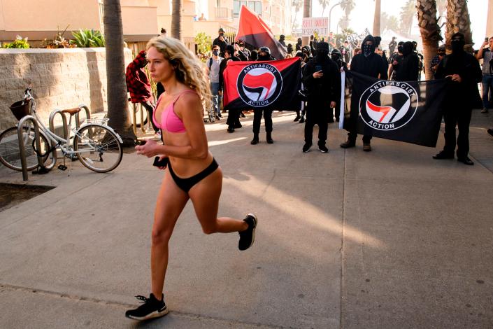 A pedestrian jogs past counter-protesters, some carrying Antifa flags, as they wait to confront a &quot;Patriot March&quot; demonstration in support of Donald Trump near the Crystal Pier on Jan. 9, 2021 in the Pacific Beach neighborhood of San Diego, California.