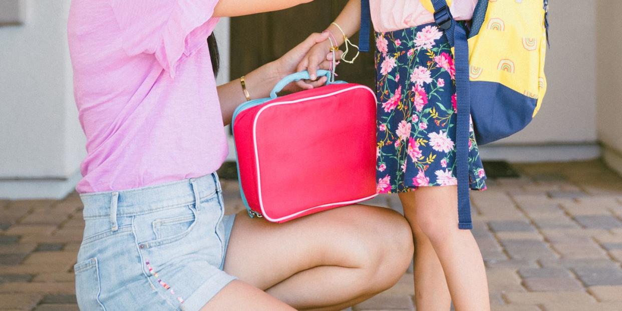 mom handing red lunch box to daughter