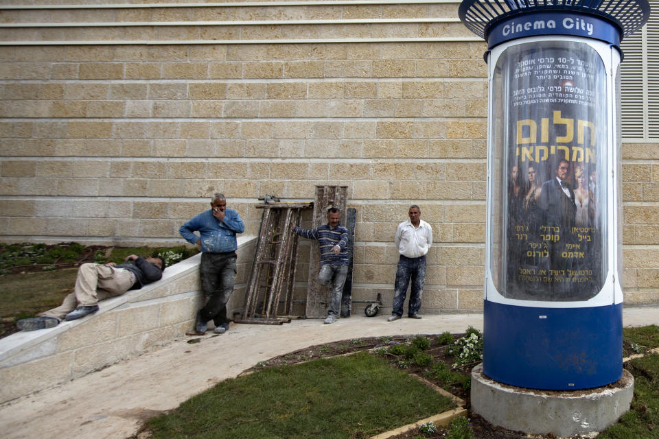 I this Thursday, Feb. 27, 2014 photo, workers stands next to a movie poster for the movie "American Hustle" translated to Hebrew as “American Dream” outside a cinema in Jerusalem. David O. Russell's crime drama "American Hustle" could be a big winner at Sunday's Academy Awards. But for the movie's many international fans, it may take a little longer to realize it. In their country, there is simply no word that captures the true essence of “Hustle.” (AP Photo/Sebastian Scheiner)